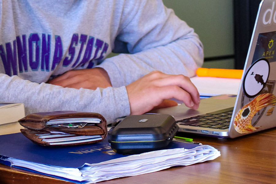 A student studies on their laptop with wallet, phone, and notebook out on the table.