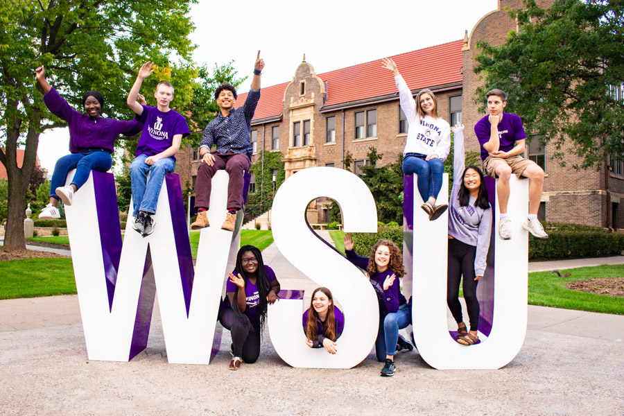 A group of students pose smiling and laughing around the WSU letters on campus.