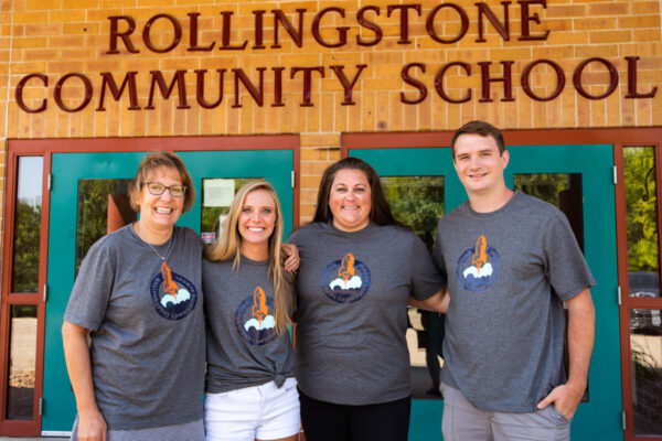 A group of WSU alumni stand in front of the Rollingstone Community School building.