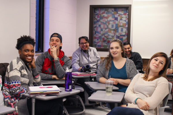 A group of students talk and laugh in a classroom.