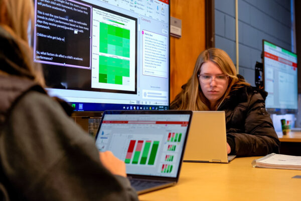 Two students analyze data on their laptops during class.