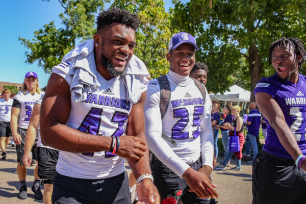 Football players laugh and smile as the walk through a crowd on their way to the football field before a game.