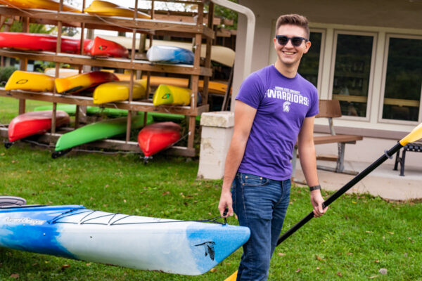 A male student pulls a kayak toward Lake Winona.