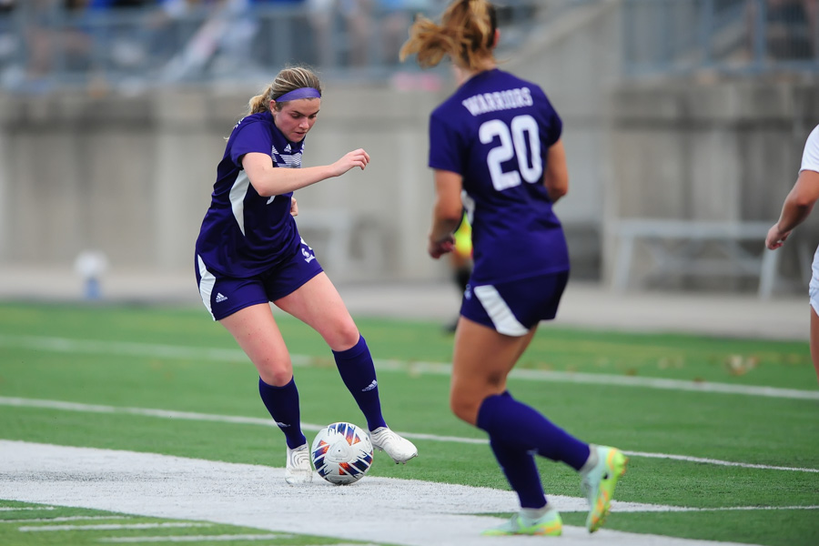 A Warriors soccer player dribbles the ball during a game.