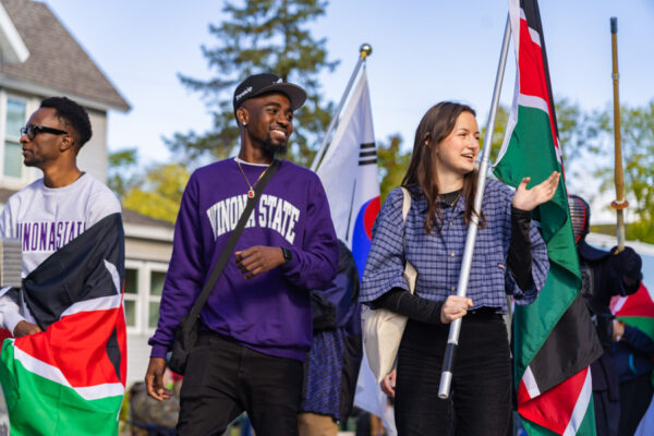 Three students march in a parade holding flags from different countries.
