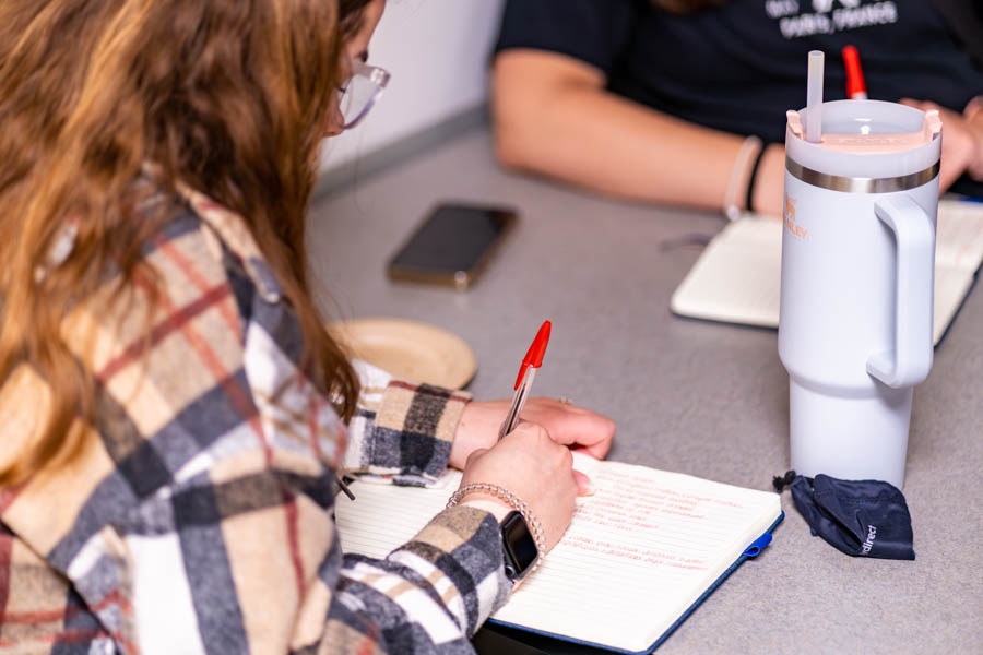 Student writing with a pen on an open notebook