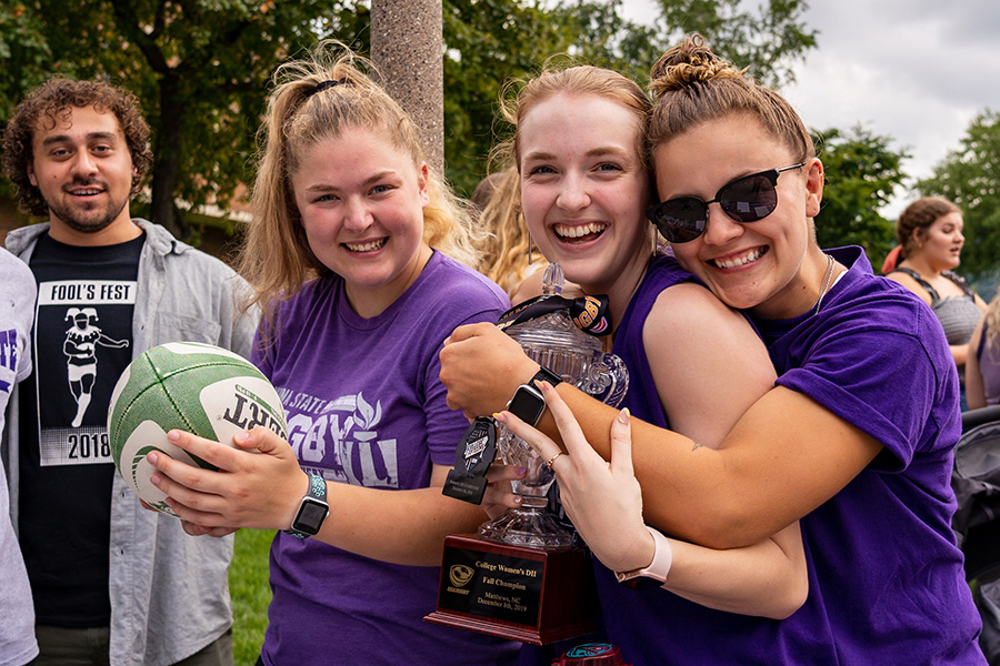 WSU rugby students hugging and holding a trophy.