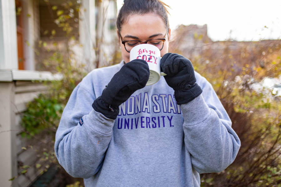 WSU student drinking from a cup and wearing mittens.