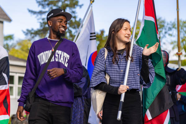 Students walk in the Winona State Homecoming Parade holding flags from international countries.
