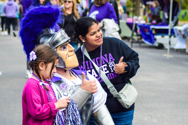 The mascot Wazoo poses with a mother and child at a campus event.