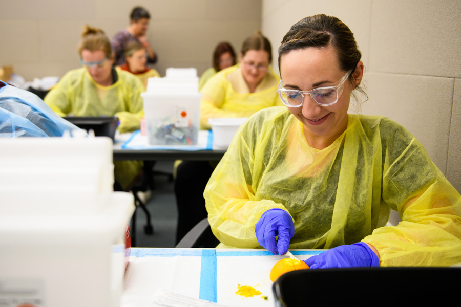 WSU student wearing scrubs, gloves, and goggles.