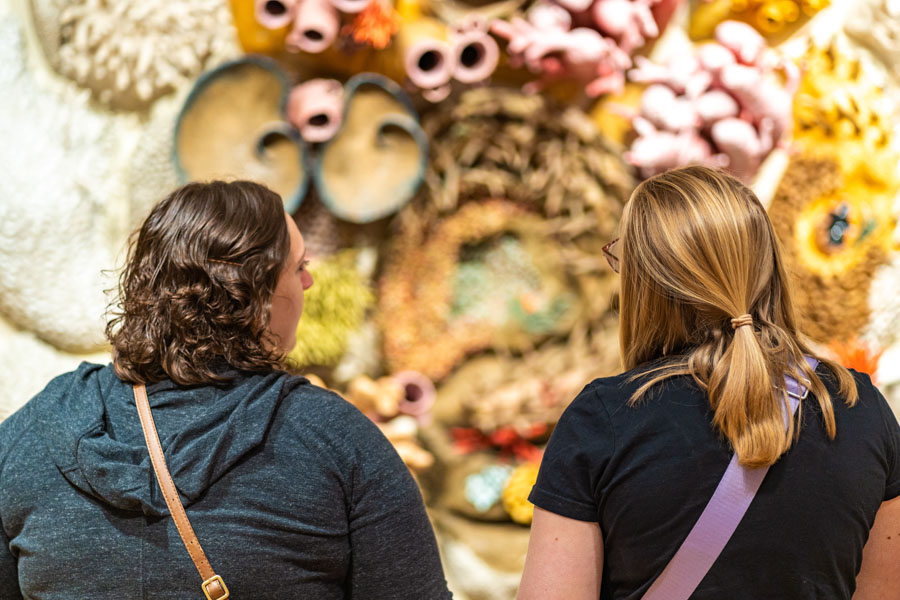 Two female students look at multi-dimensional artwork.