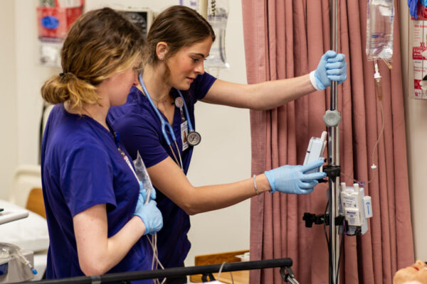 Two nursing students making adjustments on IV machine in Nursing Simulation Lab.