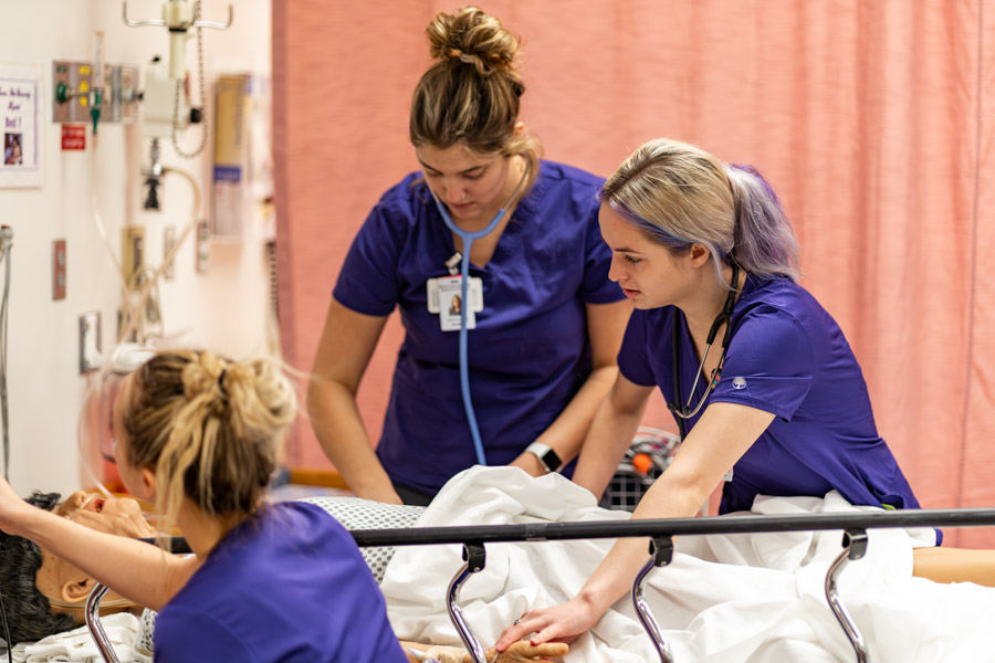 Three students working together on the nursing simulation manikin.