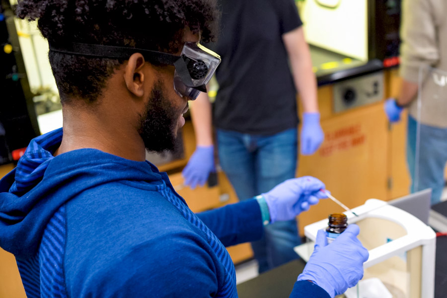 Male student wearing goggles and performing chemistry experiment.