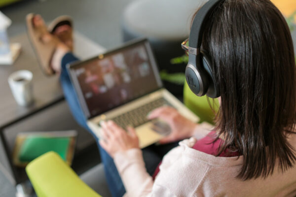 A female student wearing headphones works on a laptop in a study lounge.