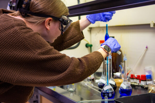 A student carefully mixes chemicals in a beaker in a lab.