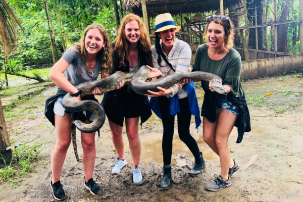 A group of students hold a giant snake at a jungle preserve while studying abroad.