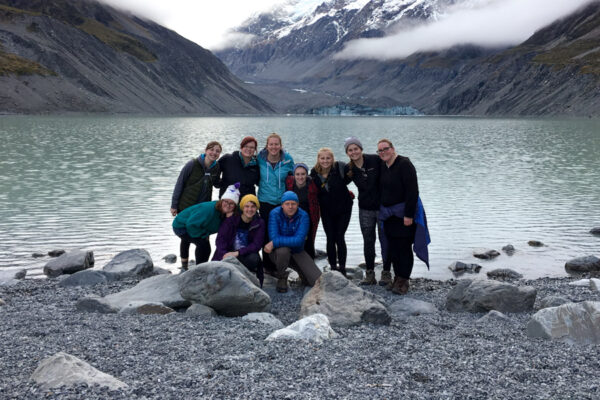 A group of WSU students pose together by a lake surrounded by mountains while on a study away trip.