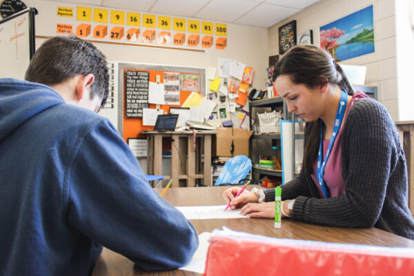 A student teacher works with a student in a classroom.