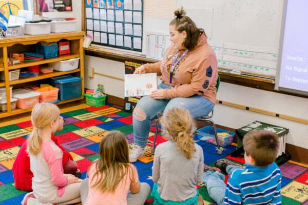 A student teacher reads to a group of kids in a classroom.