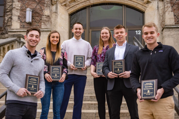 A group of students pose on the steps of Somsen Hall and show their award plaques.