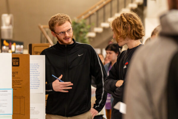 A student explains his presentation to a listener at a campus event.
