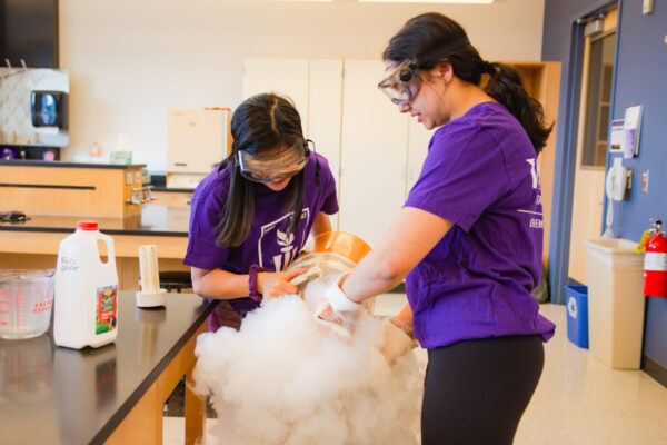 Two students create a billowing chemical reaction during a lab experiment.