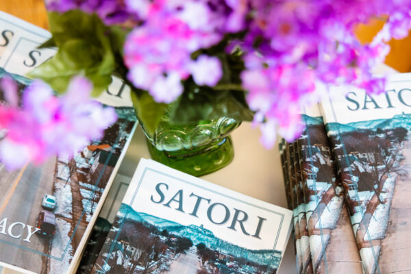 Copies of the Satori literary magazine are set out on a table with a vase of flowers.