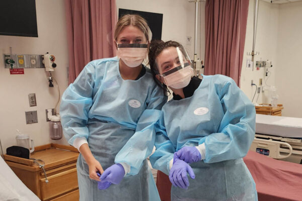Two students wearing personal protective equipment (PPE) in a nursing simulation lab.
