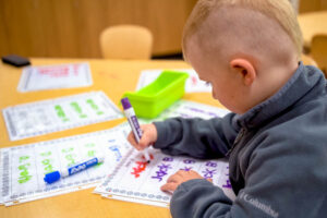 A young child writes their name with a marker