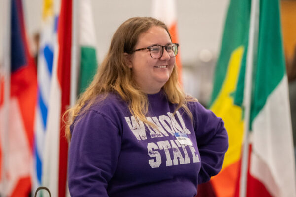 A student smiles at while standing in front of national flags from multiple countries at an event on the Winona State campus.