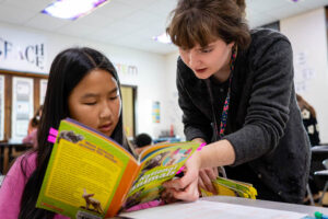 WSU student teacher in a classroom with a young child reading a book.
