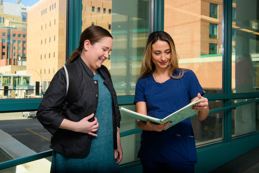WSU students, one wearing scrubs and holding a clipboard, discuss a case study at a hospital