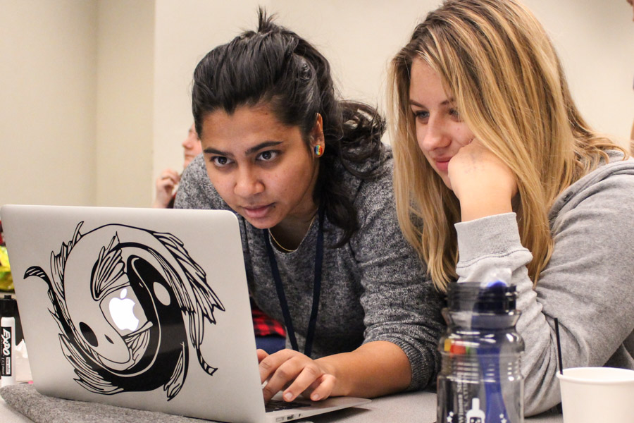 Two female WSU students work through code together on a laptop.