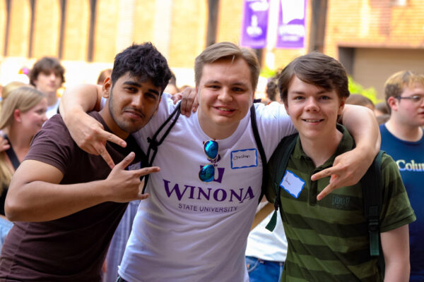 Three male students pose together smiling and flashing hand signs.