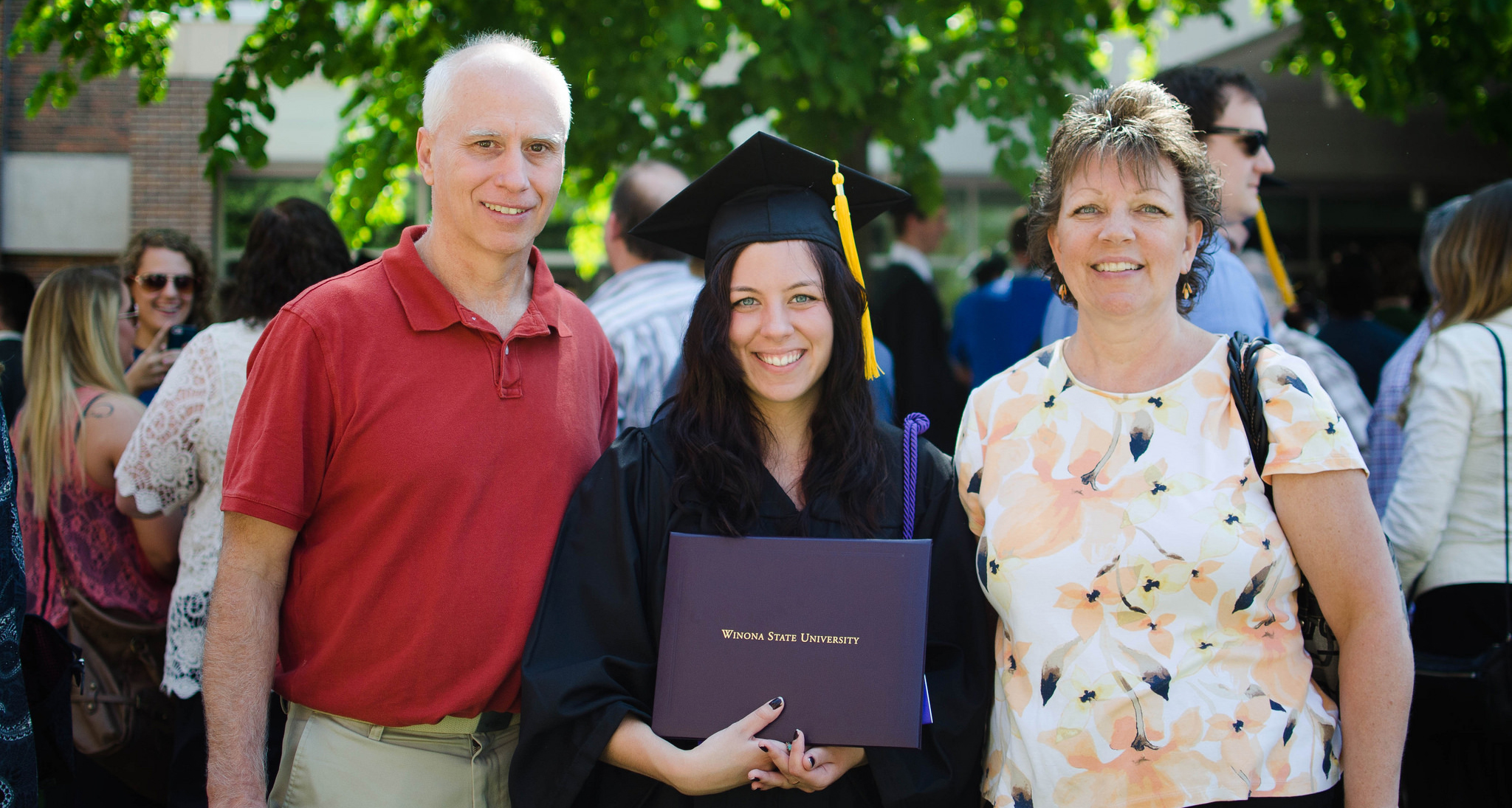 A new graduate holds her diploma and poses with her parents. 