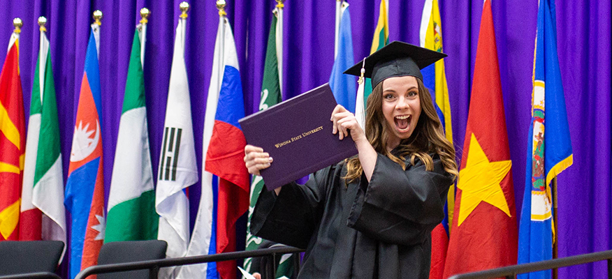 A WSU graduate smiles while showing off her diploma.