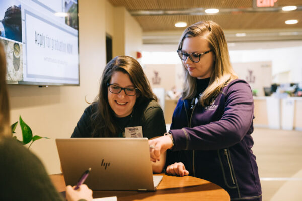 Two female students work on a laptop in the Warrior Hub.