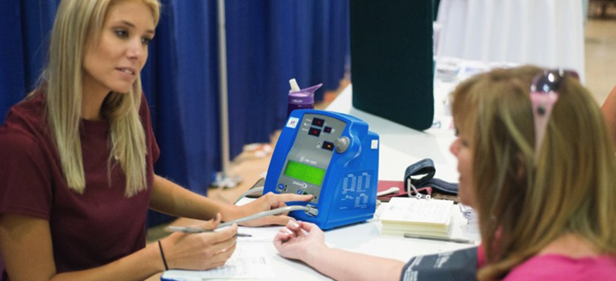 A female student tests a person's blood at a community event.