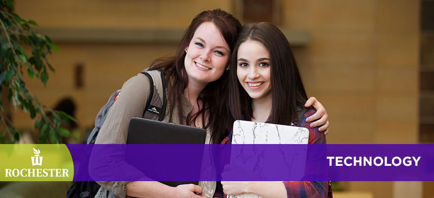 Two female students pose together holding laptops