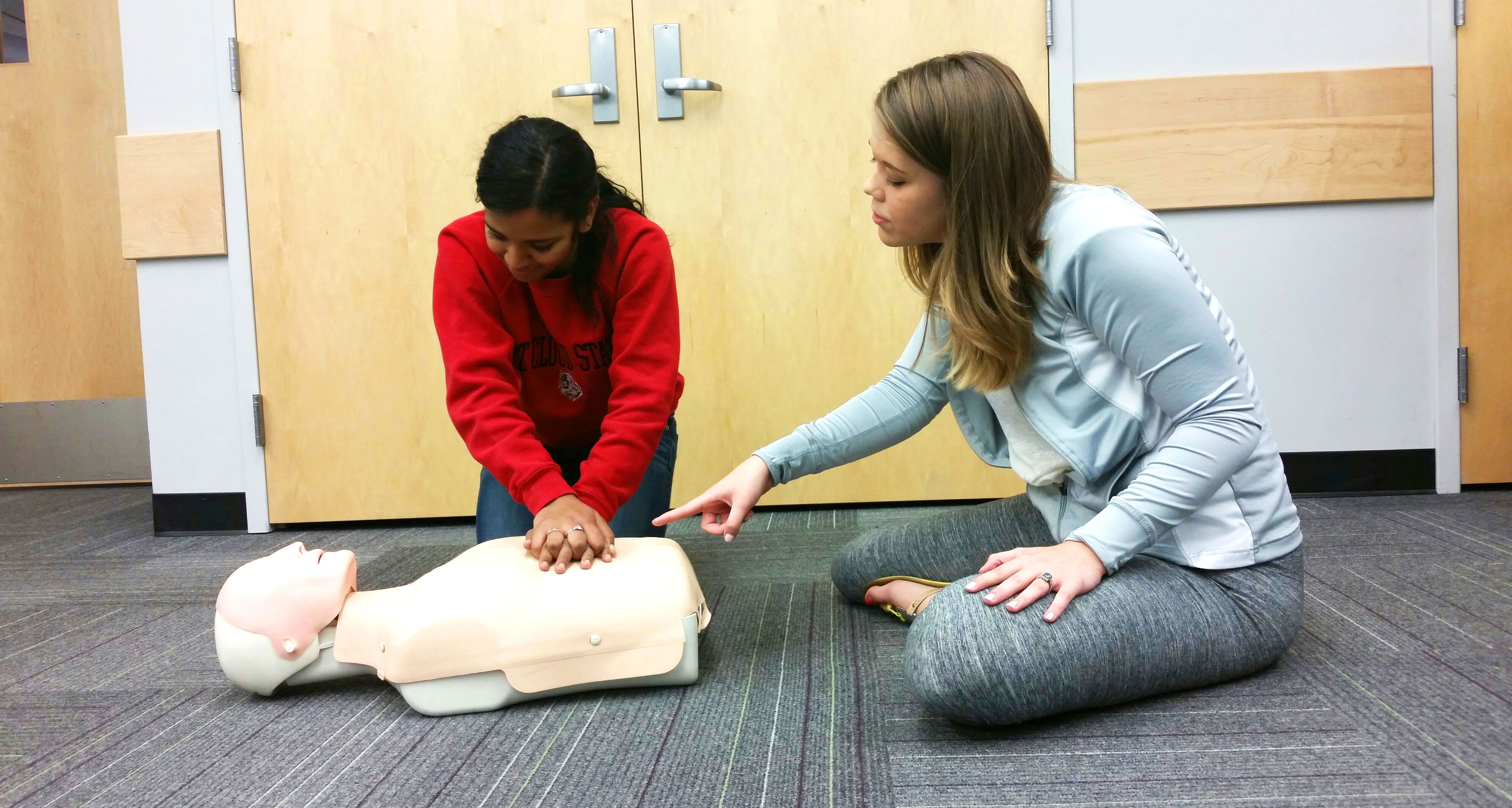 Two students practicing CPR on a CPR mannequin 