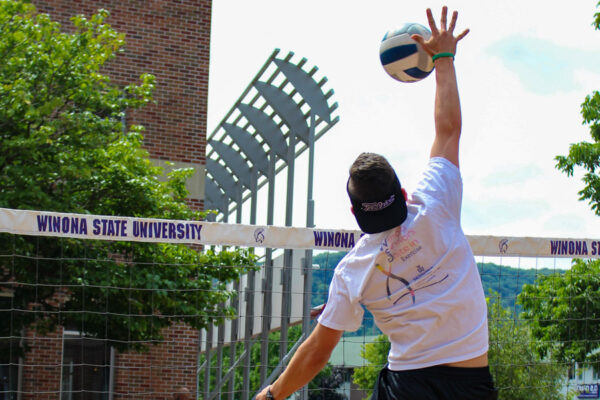 A student spikes the ball during a sand volleyball game outside Kryzsko Commons.