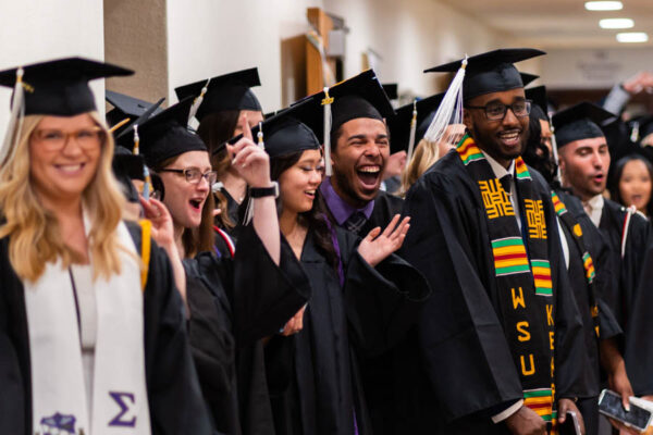 Graduates dressed in caps and gowns cheer happily.