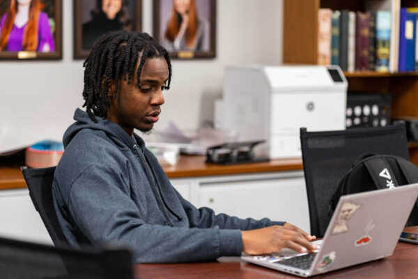 A male student works on a laptop in an office on the WSU Winona campus.