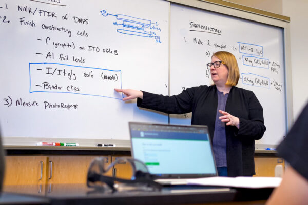 A professor writes on a whiteboard during a class lecture.