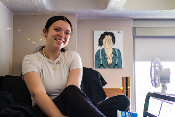 A female student smiles while sitting on a bed in a residence hall room at WSU campus.