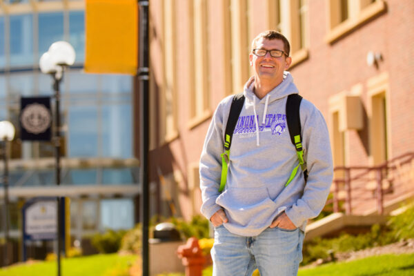 A male student wearing a WSU sweatshirt stands outside an RCTC building.