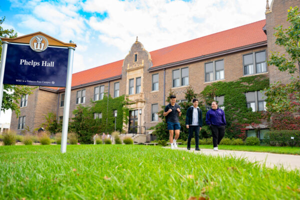 Students walk down a sidewalk in front of Phelps Hall on WSU campus.