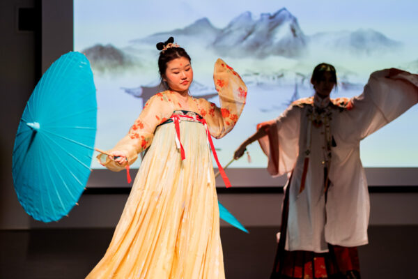 Two international students dressed in traditional cultural clothing perform a dance.